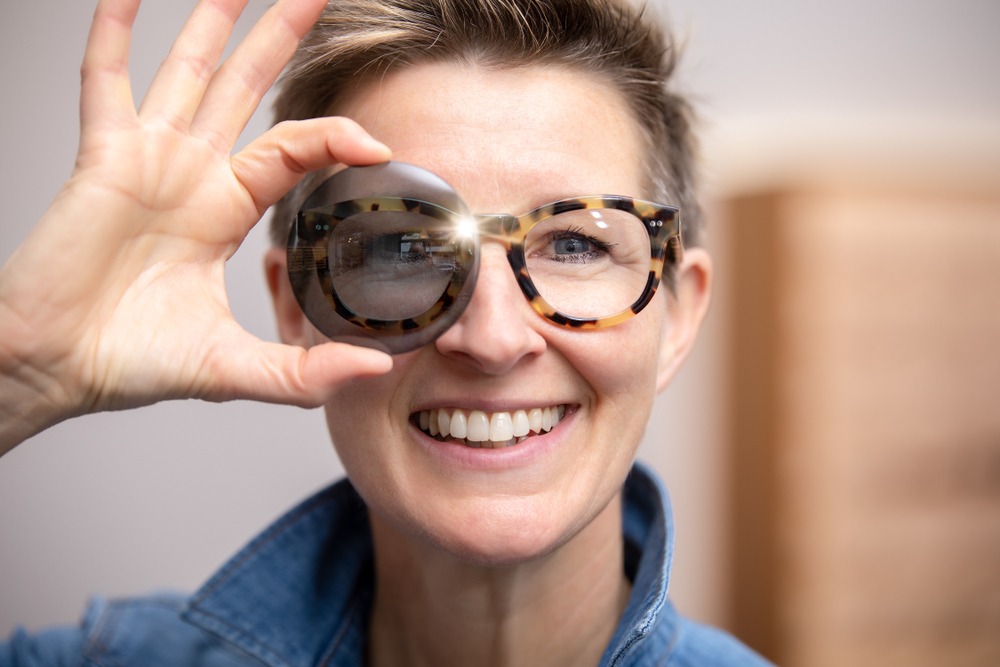 woman holding tinted lens in front of her glasses