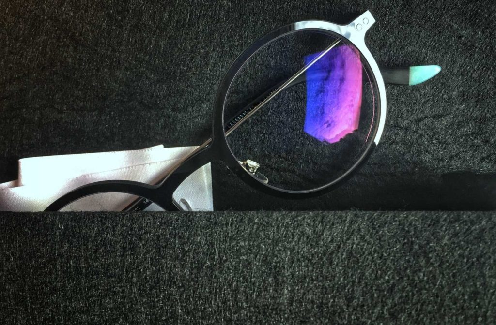 glasses on black wool with lenses reflecting blue, indigo, and violet light off the upper surface