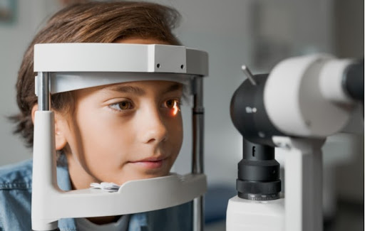 A boy with his chin resting on a tonometer receiving an eye exam from his optometrist