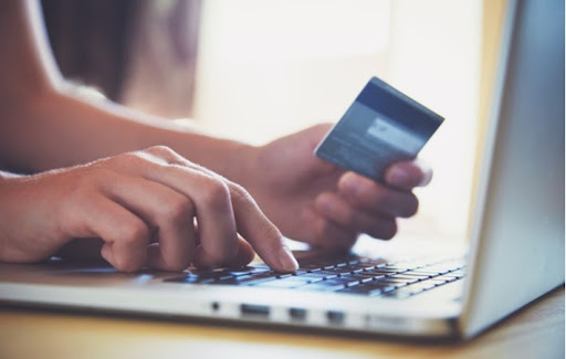 A person's hands holding a credit card while using a laptop to online shop for contact lenses