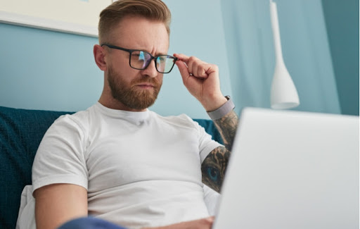 A man adjusting to new glasses squinting slightly while he looks at his laptop