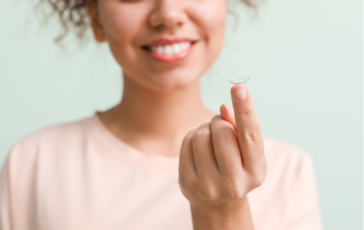 A woman reaching out her arm with a contact lens resting on her fingertip