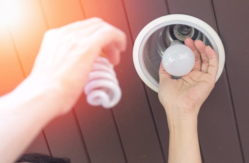 A person changing one of their light bulbs from a compact-fluorescent to an LED blub