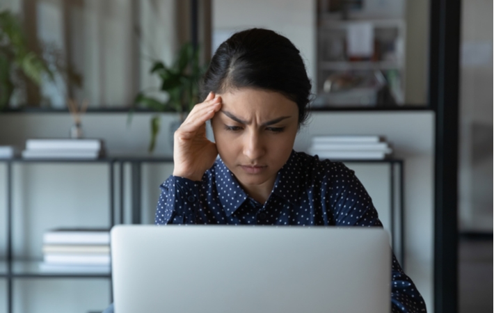 A woman using her laptop holding her forehead in pain from a headache