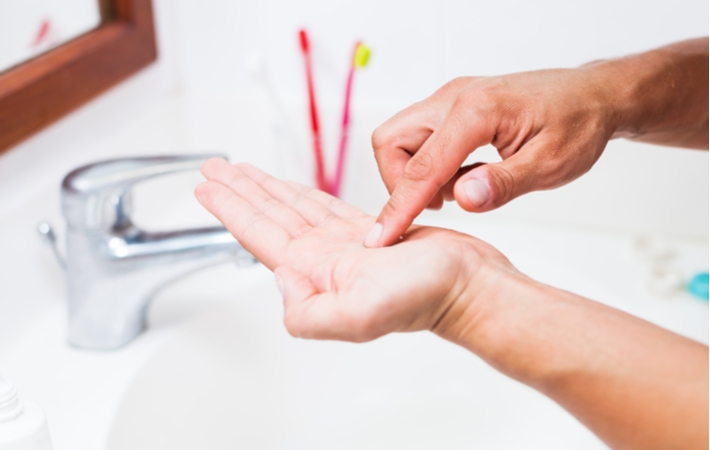 A person cleaning a contact lens with cleaning solution in the palm of their hand with their finger