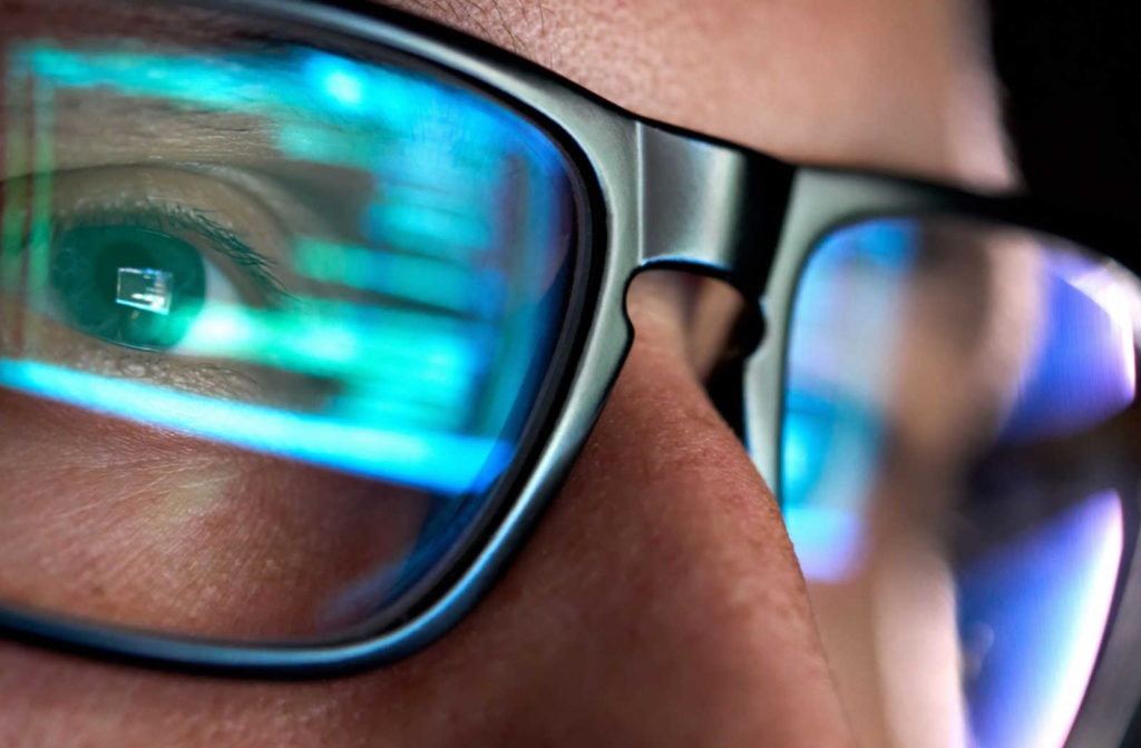A person wearing eye glasses with a digital screen reflecting on the glass.