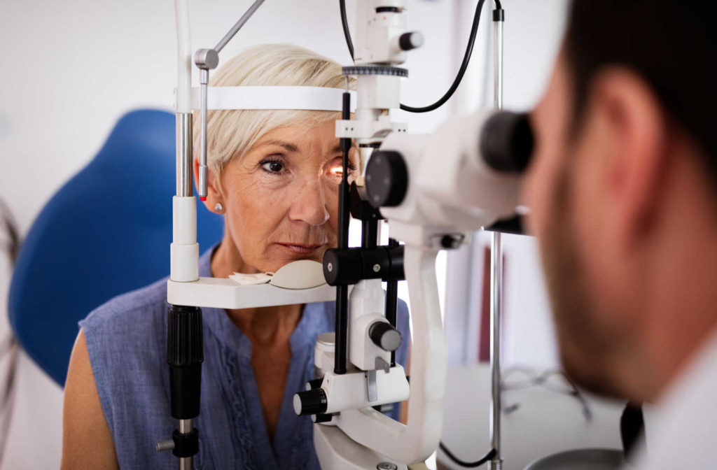 A woman seated for an eye exam and having an eye doctor examine using eye testing instrument.