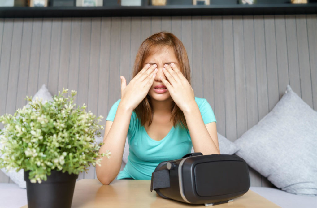 A lady in a blue-green coloured shirt with her both hands massaging her eyes after playing video games using a VR headset.