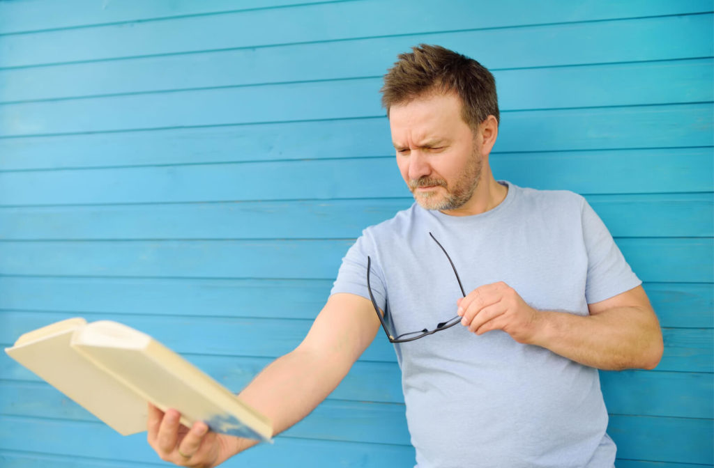 A man holding a book and unable to read clearly due to farsightedness.